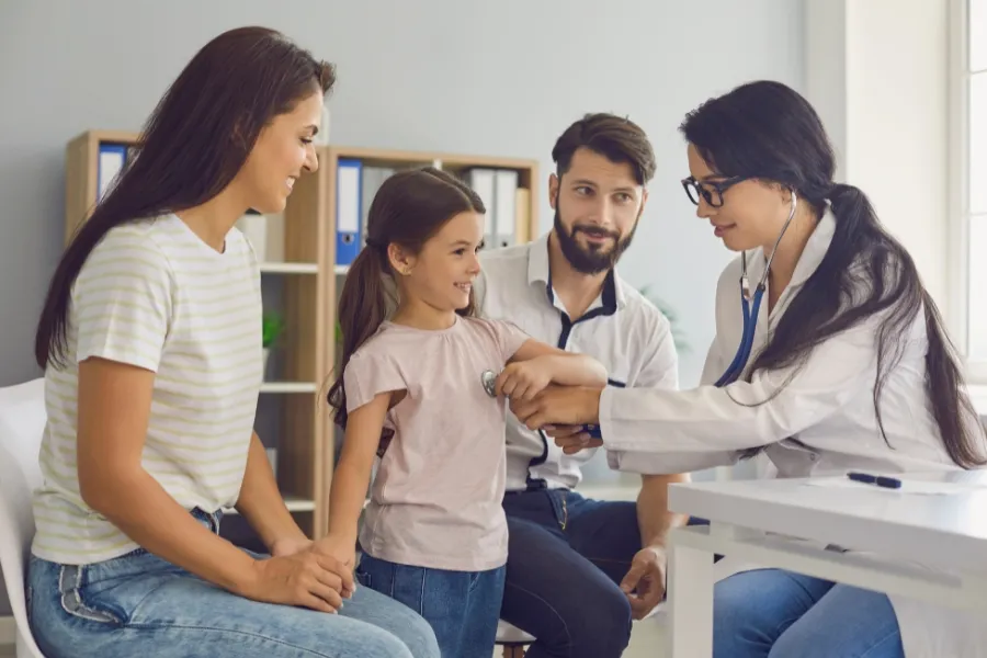 Doctora ausculta a una niña junto a sus padres en consulta; seguro de salud Adeslas en Altea